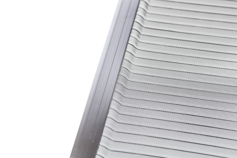 Close-up of a metallic vent or grille with evenly spaced horizontal slats and a mesh screen, photographed at an angle against a white background.